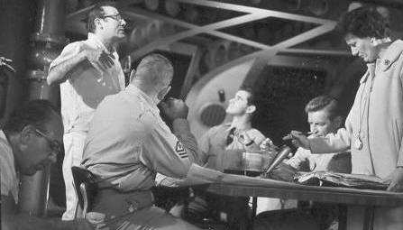 Irwin Allen discusses the upcoming take as a technician works foreground left and  script girl checks script.  Henry Kulk, Derrik Lewis and Richard Basehart seated.